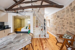Ein modernes Interieur mit freiliegenden Holzbalken, einer Steinwand, einem Essbereich mit einem Marmortisch und einer Treppe, die zu einem Schlafzimmer führt.