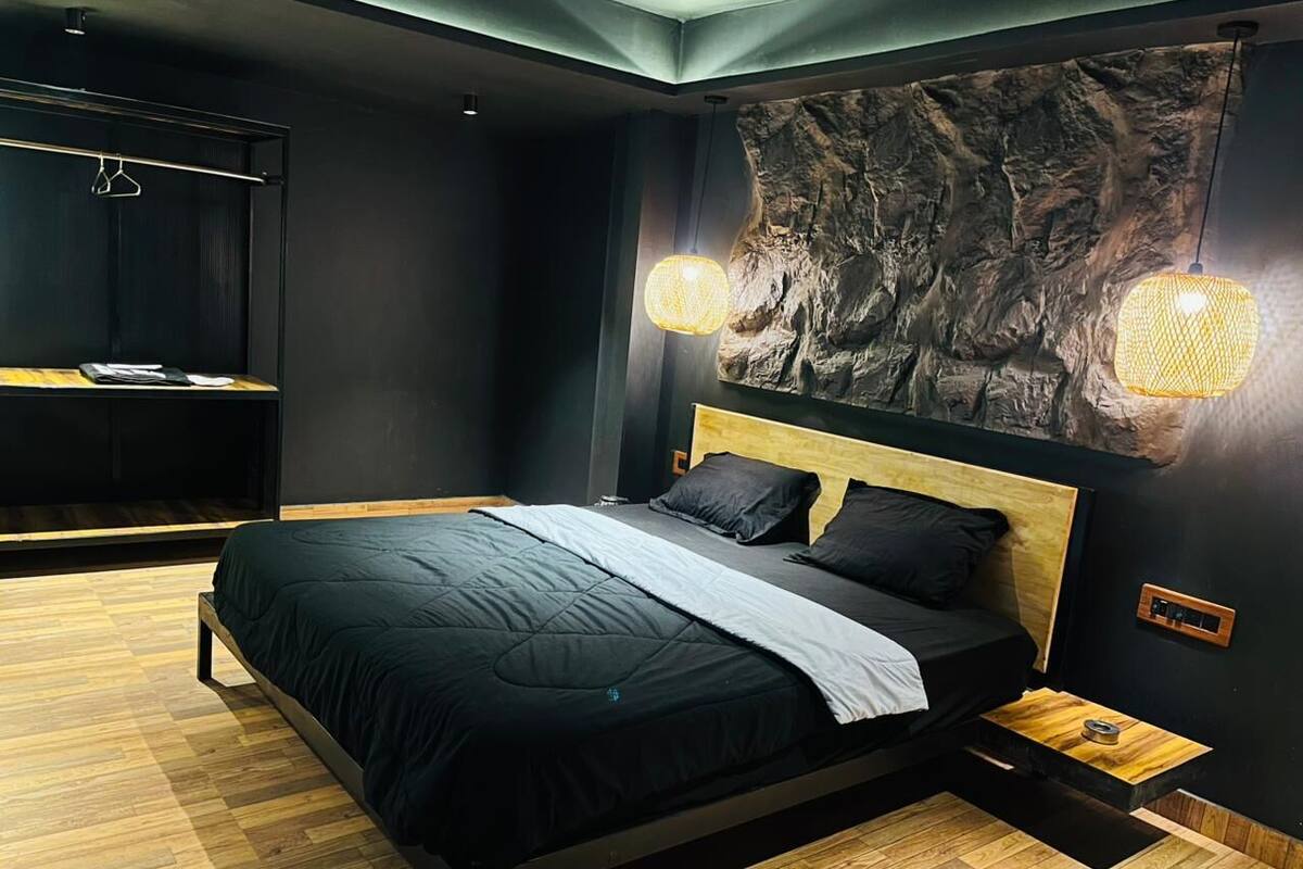 A modern bedroom with a bed, wooden flooring, a wall-mounted shelf, and a textured wall decoration.