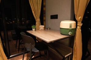 A dining area with a table, chairs, a potted plant, a decorative item, and a green and white appliance. - At Venue Groups (Kodaikanal)