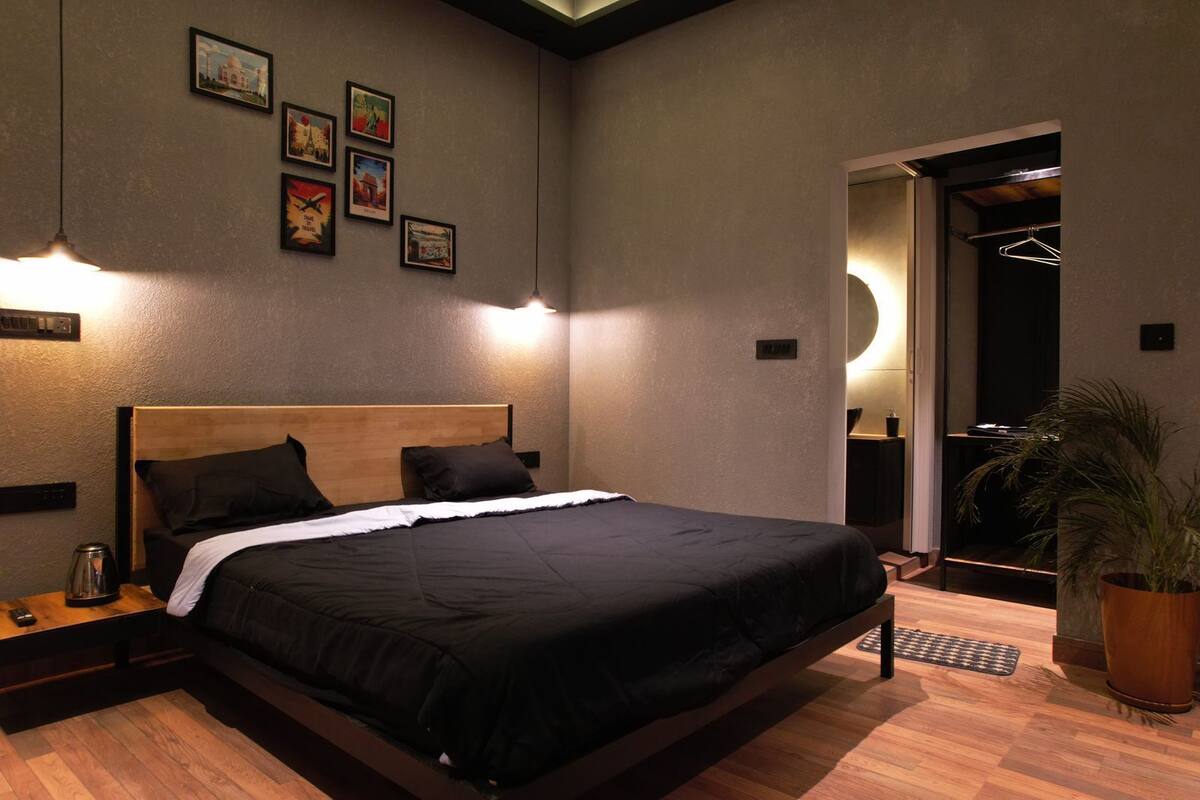 A modern hotel room with a large bed, bedside tables, a potted plant, and framed pictures on the wall.