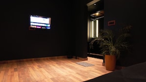Een kamer met een houten vloer, een potplant, een aan de muur bevestigd scherm en een deur naar een andere ruimte.