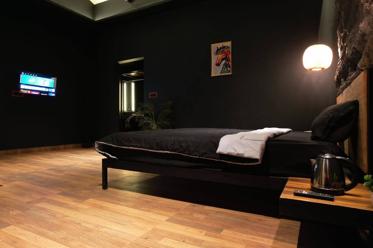 A modern bedroom with a bed, a television, a wall-mounted light, and a coffee maker.