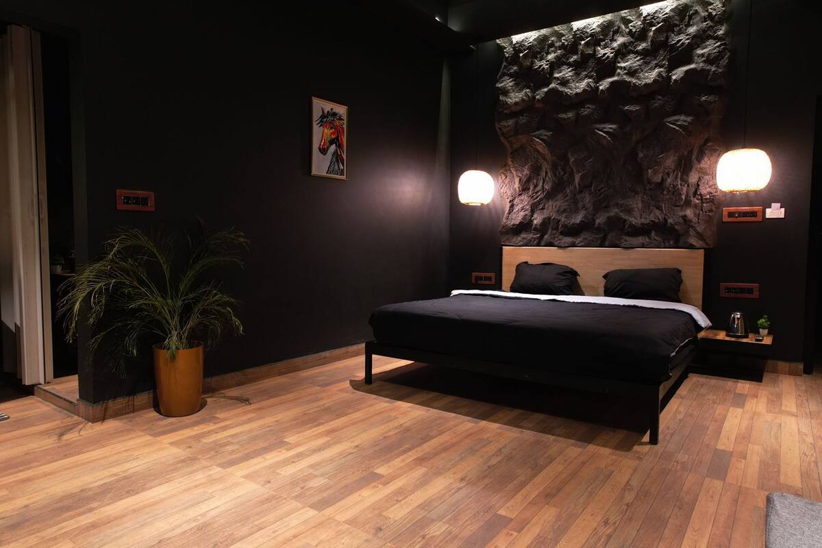 A modern bedroom with a large bed, two wall-mounted lights, a potted plant, and a rock wall mural.