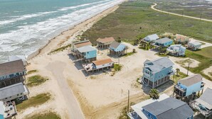Luftaufnahme einer Küstenwohngegend mit Strandhäusern, einem Sandstrand und einer Straße parallel zum Ufer.
