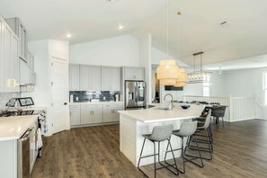 A modern kitchen with white cabinetry, a large island with bar stools, and a hanging light fixture. - Luxury 4BR Beach House with Stunning Gulf Views (Freeport)
