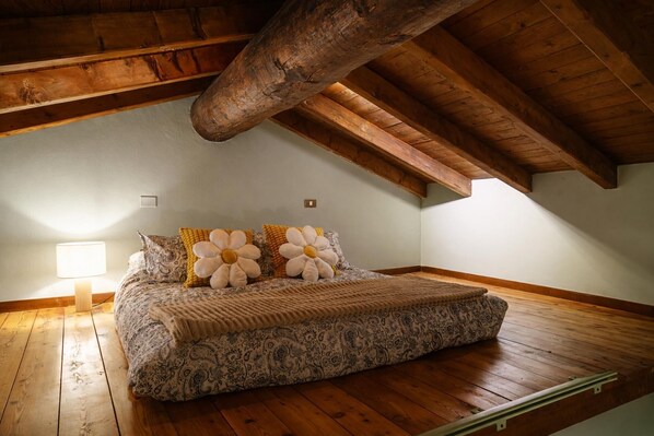 A bedroom with a wooden ceiling, a bed with floral pillows, a bedside lamp, and a patterned bedspread.