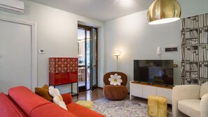 Ein Wohnzimmer mit einem roten Sofa, einem braunen Sessel, einem Fernseher und einem Bücherregal.
