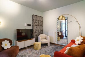 A living room with a TV, sofa, armchair, bookshelf, and a mirror.