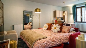 Ein Hotelzimmer mit einem großen Bett, einer Sitzecke mit einem roten Sessel, einer Küchenzeile und einem Fenster mit Vorhängen.
