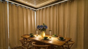 Ein Essbereich mit einem Holztisch, gedeckt für vier Personen, umgeben von Vorhängen und einer Vase mit blauen Blumen auf dem Tisch.
