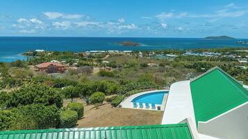 A coastal property with a swimming pool, lush greenery, and a view of the ocean.