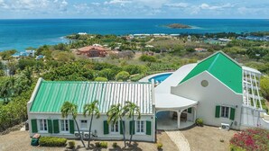 Een kustpand met zwembad, een groot huis met een groen dak en uitzicht op de oceaan.