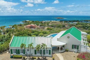 A coastal property with a swimming pool, a large house with a green roof, and a view of the ocean. - Ocean View Villa with Buck Island Views (Christiansted)