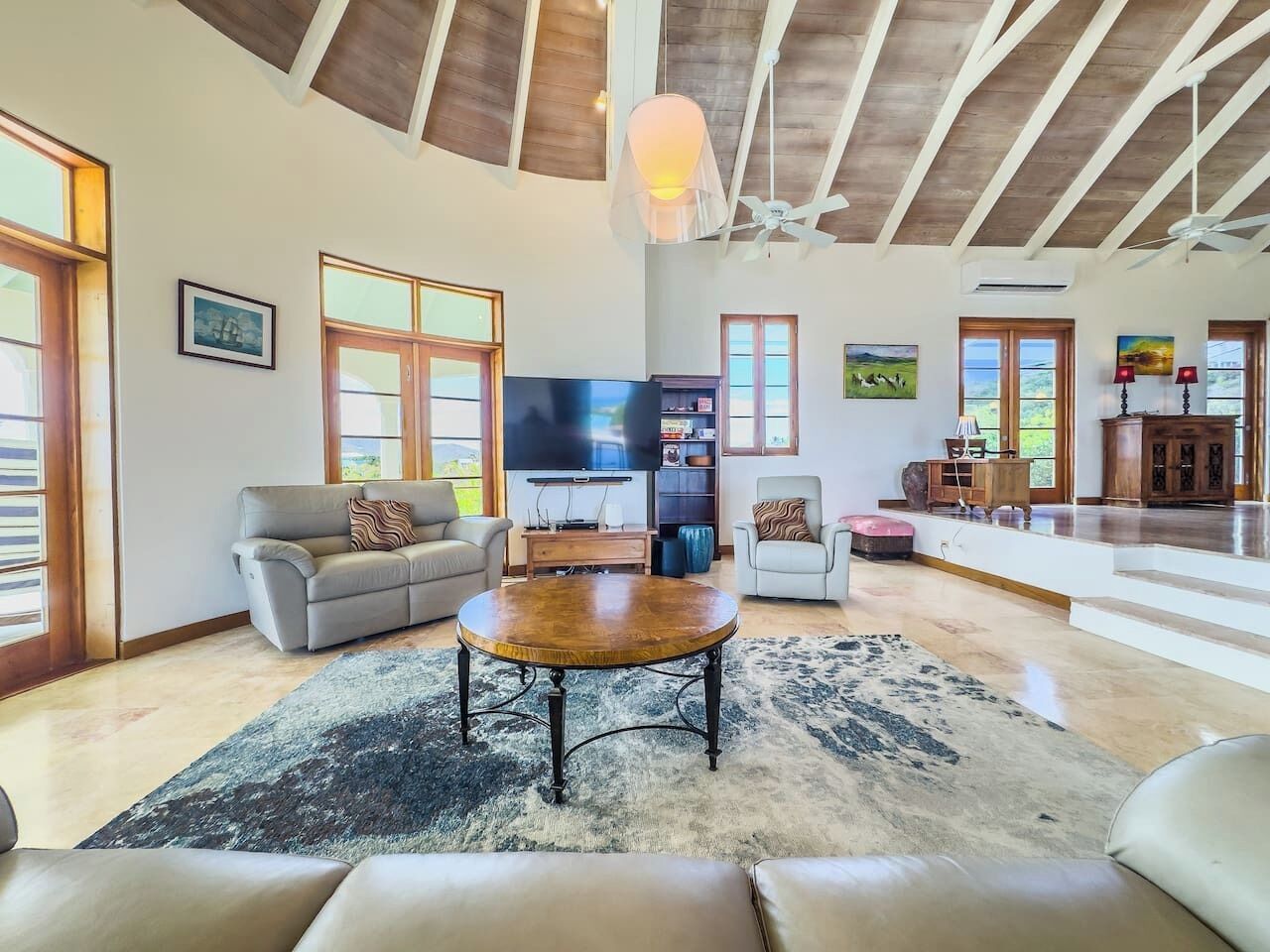 A spacious living room with a large round coffee table, sofas, and a television.