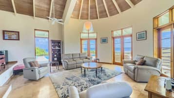 A spacious living room with a high ceiling, multiple seating areas, and large windows providing views.