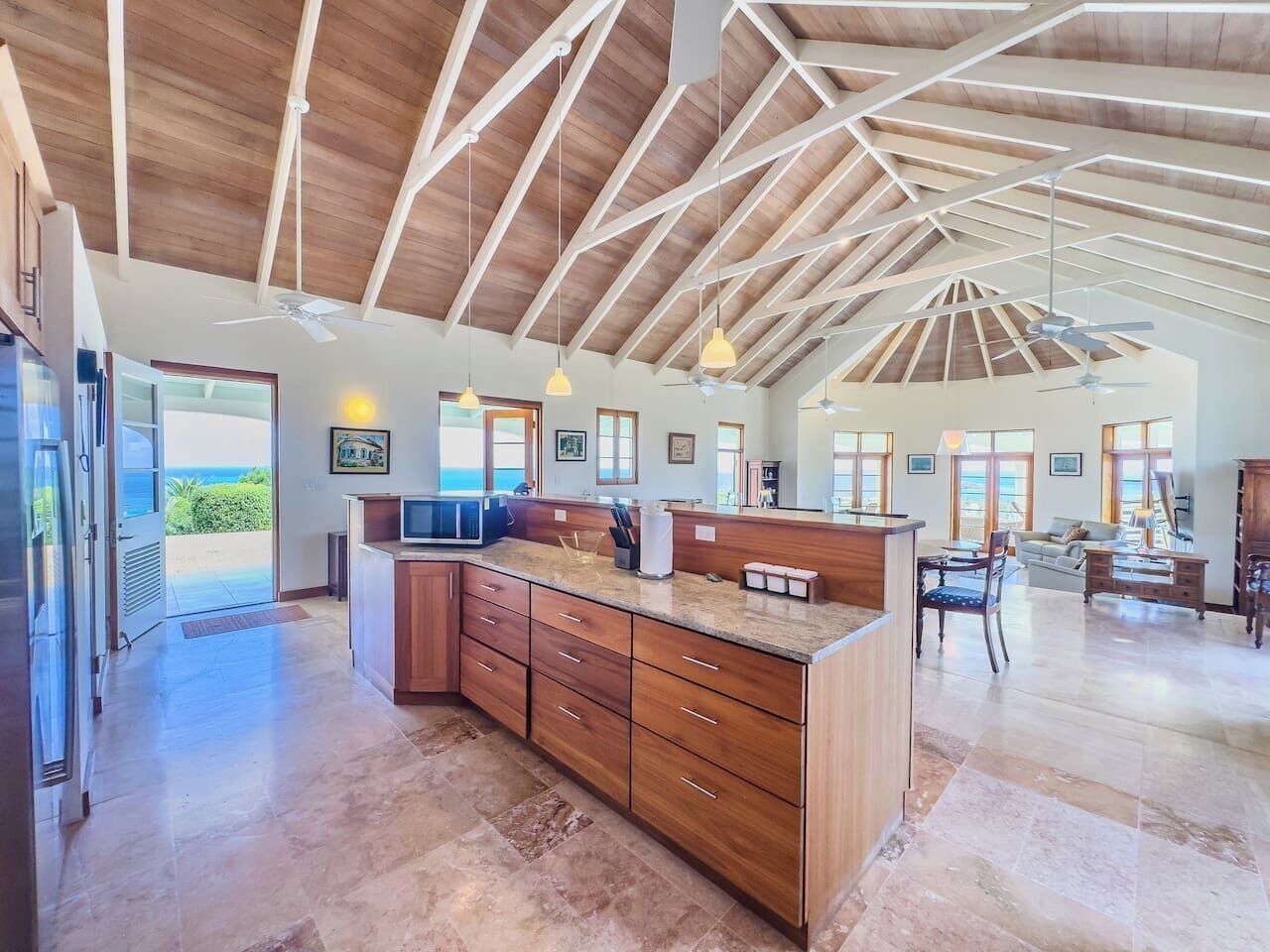 A spacious kitchen with a high ceiling and wooden beams, a large island with drawers, and a view to the outside.