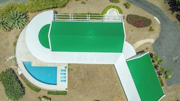 An aerial view of a property with a large green-roofed building, a swimming pool, and landscaped gardens.