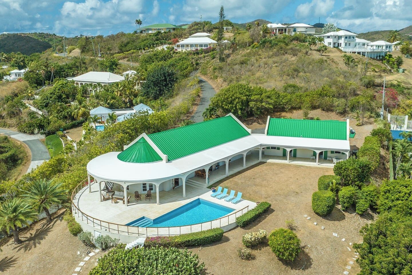 A large, white, single-story building with a green roof, a swimming pool, and a covered patio area.