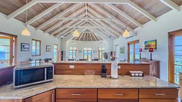 A kitchen with a large island, wooden cabinets, a microwave, and pendant lighting.
