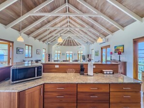 A kitchen with a large island, wooden cabinets, a microwave, and pendant lighting. - Ocean View Villa with Buck Island Views (Christiansted)