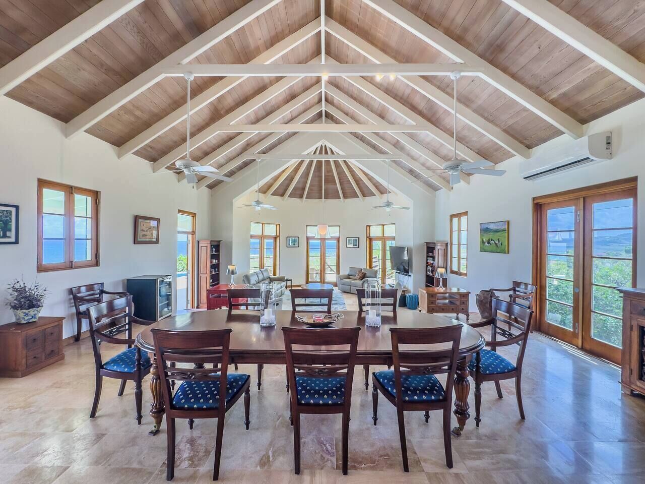 A spacious dining area with a high ceiling and wooden beams, surrounded by large windows and a view of the outdoors.