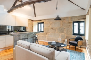 A modern kitchen with a stone wall, a bar area, and a seating area with a sofa and chairs. - Albertina Mezzanine 4 Studio (Porto)