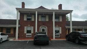 A two-story brick building with a central entrance, a covered porch, and a parking lot with two cars. - DOVER INN (Dover)