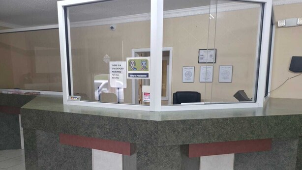 A reception desk with a glass partition, a sign indicating a $100 deposit for rooms, and a 'Sorry No Pets Allowed' sign. - DOVER INN (Dover)