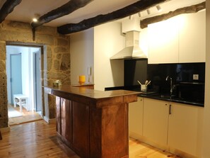 A kitchen with a wooden island, white cabinets, and a stone wall. - Albertina 1 BR with Terrace (Porto)
