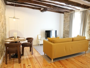 A furnished living room with a sofa, a dining table with chairs, a television, and a stone wall. - Albertina 1 BR with Terrace (Porto)