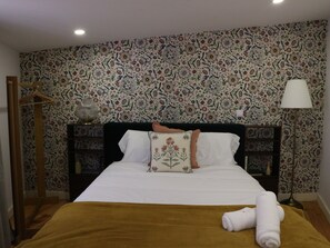 A hotel room with a patterned wallpaper, a bed with white linens, a brown throw blanket, and a rolled towel on the bed. - Albertina 1 BR with Terrace (Porto)