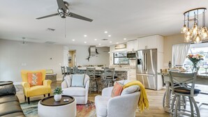 Una sala moderna con sofá, sillón y mesa de centro, una cocina con electrodomésticos de acero inoxidable y un comedor con candelabro.