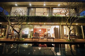 A modern building with a pool, outdoor seating, and a visible interior with furniture and plants. - 3BR villa in tranquil Hoi An Vietnam, private pool, pick-up&breakfasts inclusive (Đà Nẵng)