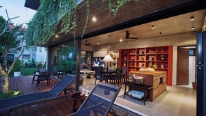 Een moderne keuken met rode planken, een eethoek met stoelen en een houten terras met een loungestoel.
