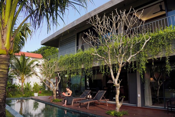 A modern building with a pool, lounge chairs, and a tree in the foreground. - 3BR villa in tranquil Hoi An Vietnam, private pool, pick-up&breakfasts inclusive (Đà Nẵng)