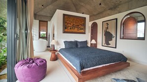 Een slaapkamer met een groot bed, een paarse relaxfauteuil en een schilderij aan de muur.