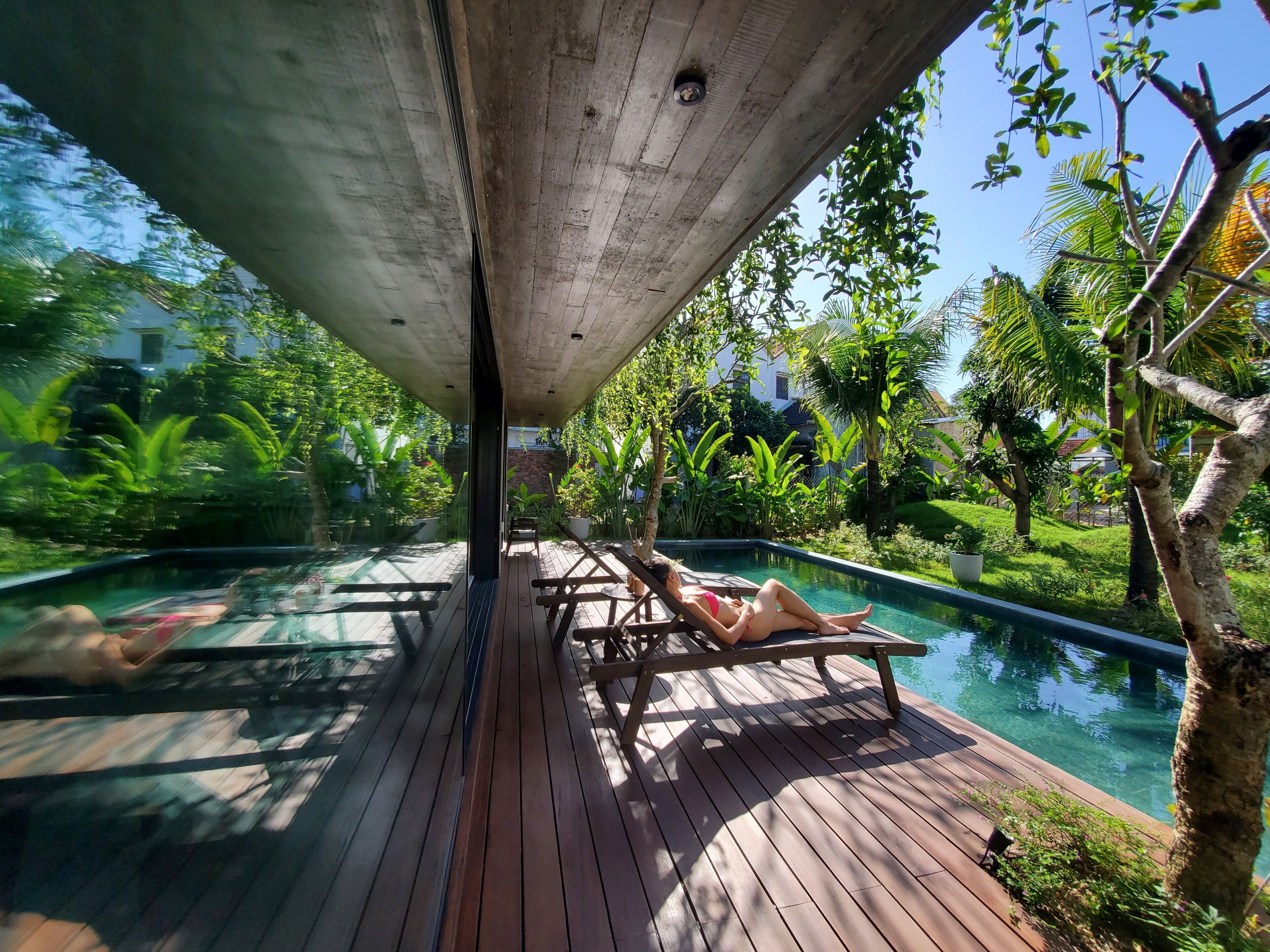 A wooden deck with a pool, surrounded by lush greenery and a clear sky.