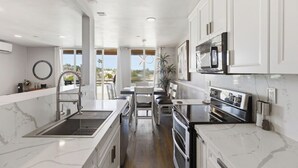 A modern kitchen with white cabinetry, a built-in oven, and a large window offering a view. - Oceanfront Oasis in Pacific Beach  Walk to PB Pier  Pool Monthly Rental (San Diego)