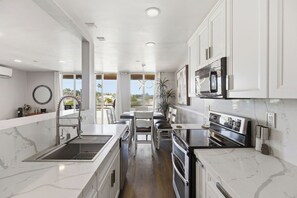 A modern kitchen with white cabinetry, a built-in oven, and a large window offering a view. - Oceanfront Oasis in Pacific Beach  Walk to PB Pier  Pool Monthly Rental (San Diego)