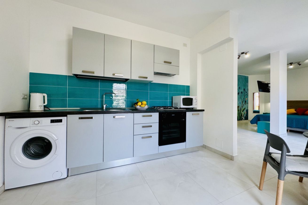 A compact kitchen with a washing machine, microwave, and a small countertop with fruits.