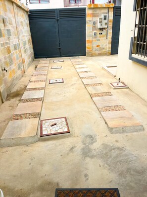 A courtyard with a tiled floor, a closed gate, and a wall with electrical boxes. - Cosy air-conditioned studio with wifi, near city center and airport - Cotonou (Cotonou)
