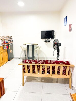 A room with a wooden bench, a small table, a television, and a fan. - Cosy air-conditioned studio with wifi, near city center and airport - Cotonou (Cotonou)
