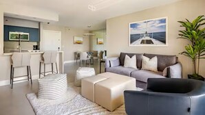 Een moderne woonkamer met een bank, voetenbankjes, een salontafel en een eethoek met stoelen en een tafel.