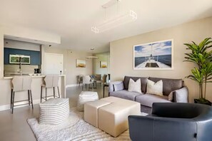 Ein modernes Wohnzimmer mit einer Couch, Hocker, einem Couchtisch und einem Essbereich mit Stühlen und einem Tisch.