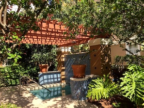 Ein Poolbereich mit einer Pergola, Kübelpflanzen und einer Wand mit Mosaikfliesen.