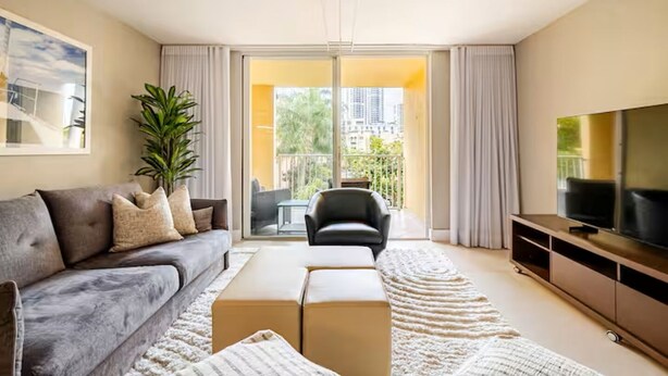 Een moderne woonkamer met een bank, een salontafel, een televisie en een balkon met gordijnen.