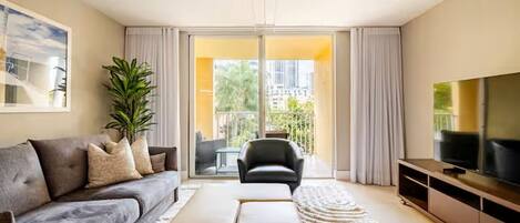 A modern living room with a sofa, a coffee table, a TV, and a balcony with curtains.