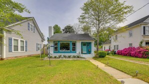 A two-story house with a blue door and windows, a front yard with a pathway, and a neighboring house with pink flowers. - Walkable Escape in Dtwn Burgaw! Quiet Home w/ Yard (Burgaw)