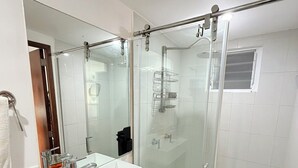 Une salle de bain moderne avec une douche à l’italienne en verre, un lavabo blanc avec un meuble noir et un grand miroir.
