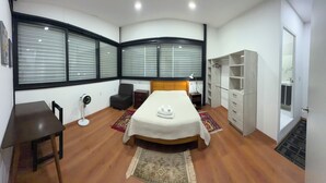Une chambre à coucher comprenant un lit, un bureau, une chaise, une armoire et une fenêtre avec des stores.